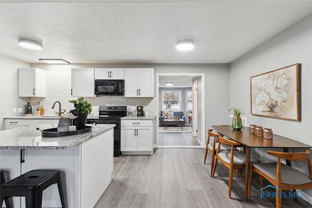 kitchen with light stone countertops, backsplash, light hardwood / wood-style floors, white cabinets, and black appliances