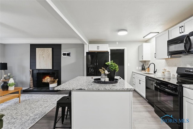 kitchen featuring black appliances, a center island, white cabinets, and a fireplace