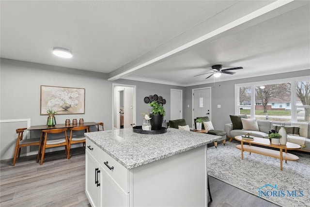 kitchen with a center island, white cabinets, light hardwood / wood-style flooring, ceiling fan, and light stone counters