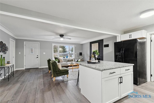 kitchen with black refrigerator with ice dispenser, ceiling fan, a kitchen island, light hardwood / wood-style floors, and white cabinetry