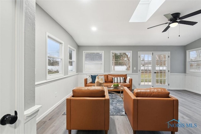 living room with french doors, light hardwood / wood-style floors, lofted ceiling with skylight, and ceiling fan