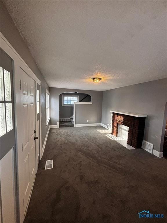 unfurnished living room featuring a fireplace, a textured ceiling, and dark colored carpet