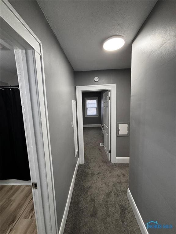 hallway with dark carpet and a textured ceiling