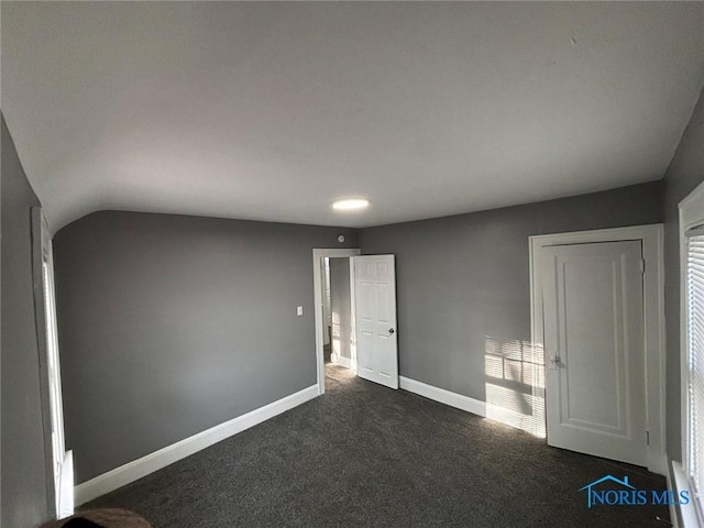 unfurnished bedroom with dark colored carpet and lofted ceiling