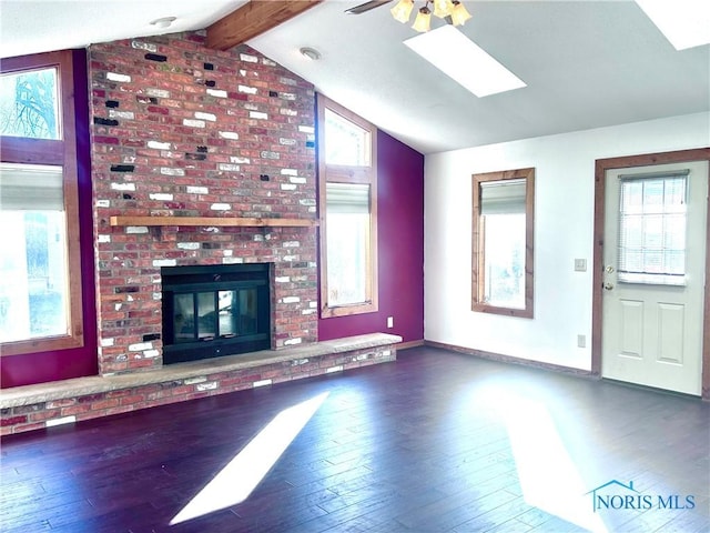 unfurnished living room with a brick fireplace, lofted ceiling with skylight, ceiling fan, and dark wood-type flooring