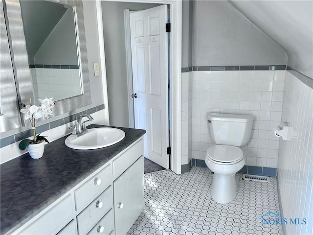 bathroom featuring tile patterned flooring, vaulted ceiling, toilet, vanity, and tile walls