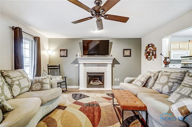 living room featuring ceiling fan, light hardwood / wood-style floors, and a tiled fireplace