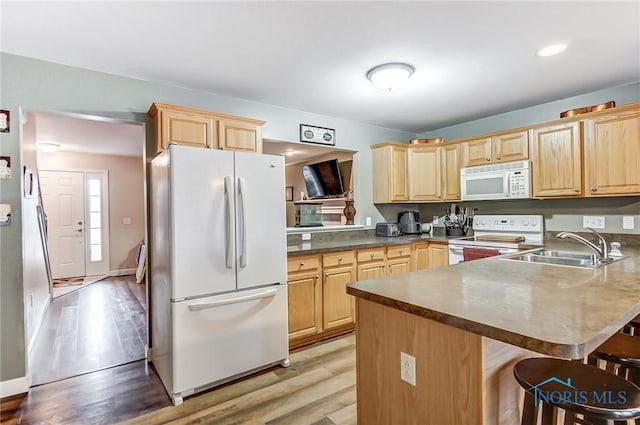 kitchen featuring white appliances, sink, light hardwood / wood-style flooring, a kitchen bar, and kitchen peninsula