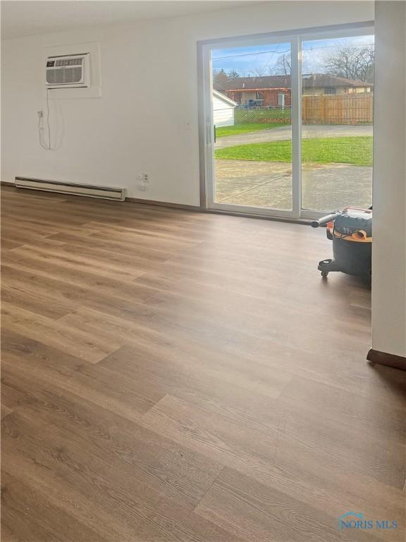 spare room with baseboard heating, a wall mounted AC, and hardwood / wood-style flooring