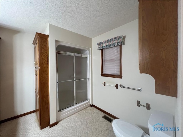 bathroom featuring a shower with door, a textured ceiling, and toilet