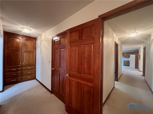 corridor with light carpet and a textured ceiling