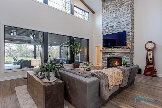 living room featuring beam ceiling, a stone fireplace, high vaulted ceiling, and hardwood / wood-style flooring