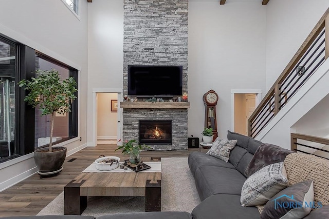 living room with hardwood / wood-style floors, a stone fireplace, and a towering ceiling