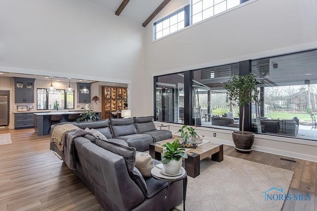 living room with beam ceiling, hardwood / wood-style floors, a towering ceiling, and a healthy amount of sunlight