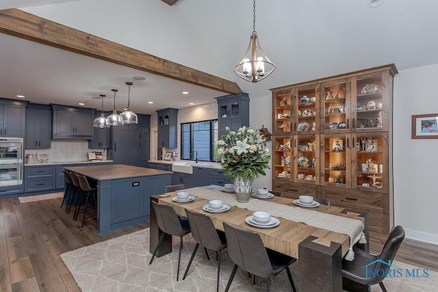 dining room featuring high vaulted ceiling, an inviting chandelier, sink, hardwood / wood-style flooring, and beamed ceiling