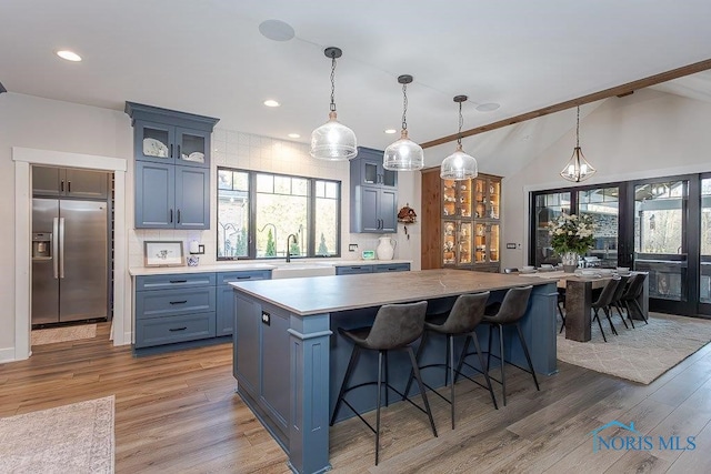 kitchen featuring blue cabinetry, tasteful backsplash, decorative light fixtures, a kitchen island, and stainless steel fridge with ice dispenser