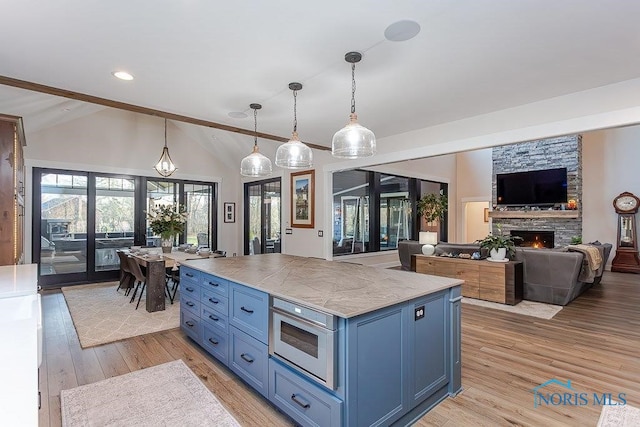 kitchen with vaulted ceiling with beams, blue cabinets, decorative light fixtures, a fireplace, and light wood-type flooring