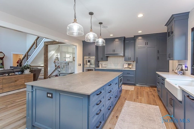 kitchen featuring tasteful backsplash, double oven, decorative light fixtures, light hardwood / wood-style floors, and a kitchen island