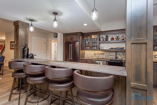 bar featuring light stone countertops, stainless steel appliances, light hardwood / wood-style floors, decorative light fixtures, and dark brown cabinets