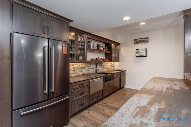 kitchen featuring sink, light wood-type flooring, high quality fridge, tasteful backsplash, and dark brown cabinets