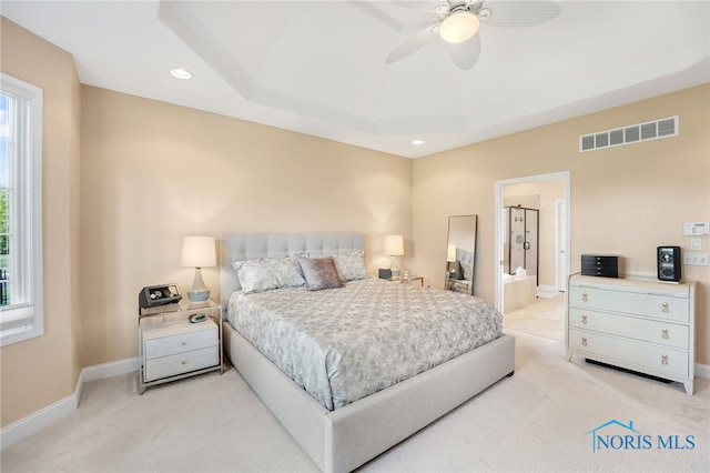 carpeted bedroom featuring ceiling fan, a raised ceiling, connected bathroom, and multiple windows