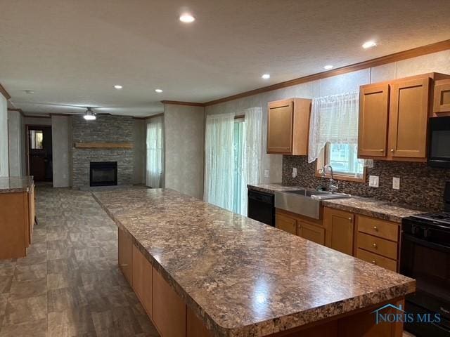 kitchen featuring a center island, black appliances, a stone fireplace, sink, and ornamental molding