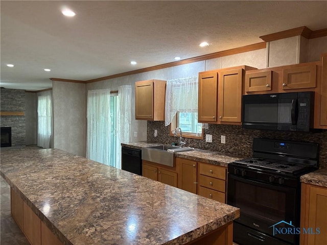 kitchen featuring crown molding, sink, black appliances, a center island, and a stone fireplace