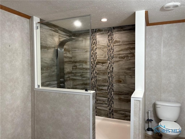 bathroom featuring toilet, a tile shower, and a textured ceiling