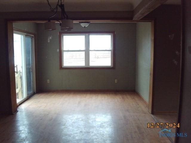 empty room with a notable chandelier, plenty of natural light, and light hardwood / wood-style flooring