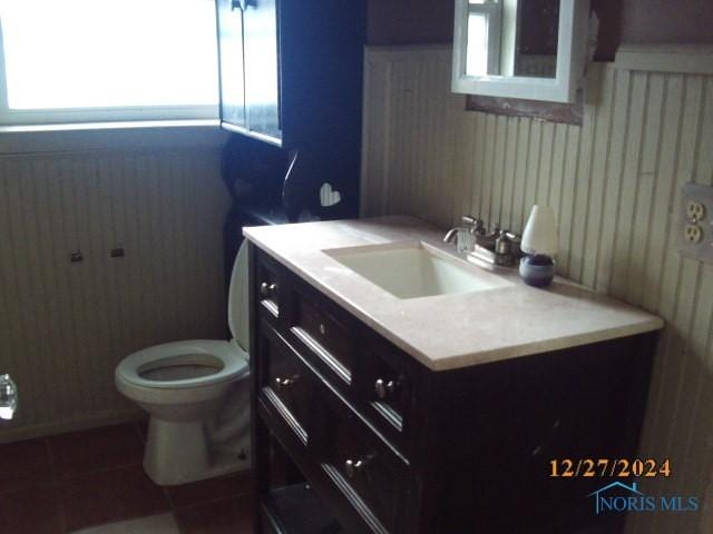 bathroom with tile patterned floors, vanity, wood walls, and toilet