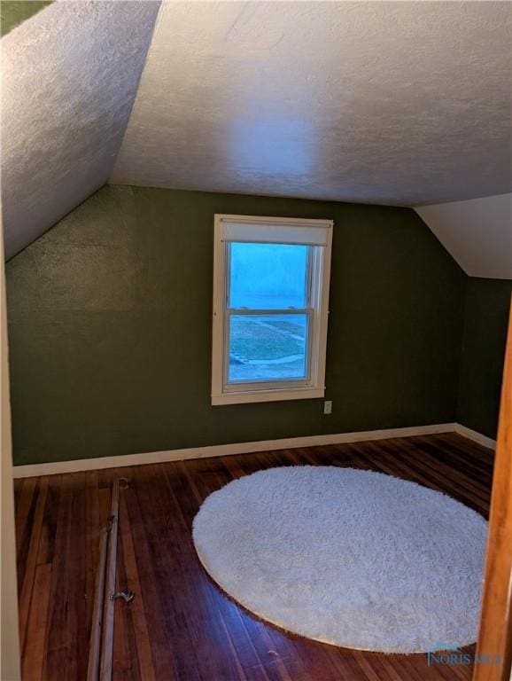 additional living space with dark hardwood / wood-style flooring, a textured ceiling, and vaulted ceiling