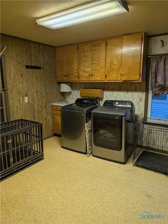 clothes washing area with cabinets, separate washer and dryer, and wooden walls