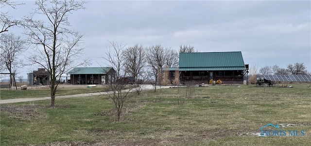 view of front of property featuring a rural view, metal roof, solar panels, and a front yard