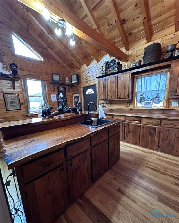 kitchen featuring wooden counters, a sink, high vaulted ceiling, wooden ceiling, and wooden walls