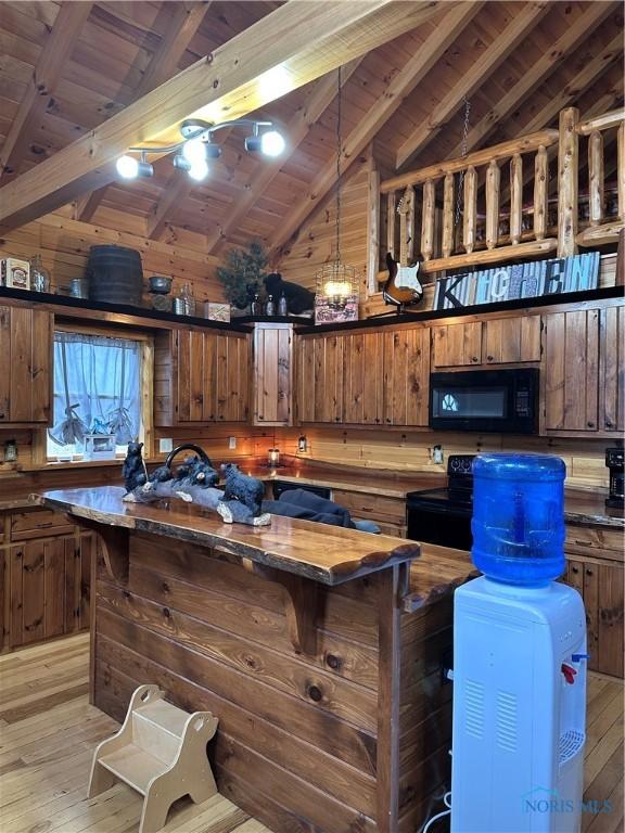 interior space with dark countertops, light wood-style floors, a center island, lofted ceiling with beams, and black appliances