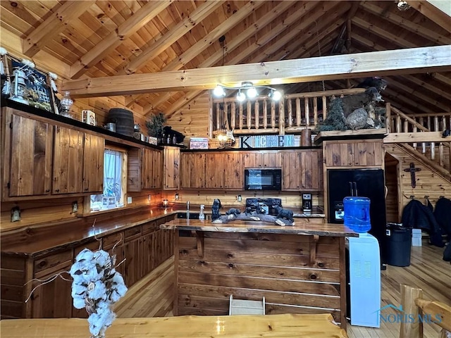 kitchen with wood walls, wooden ceiling, black appliances, light wood-style floors, and vaulted ceiling with beams