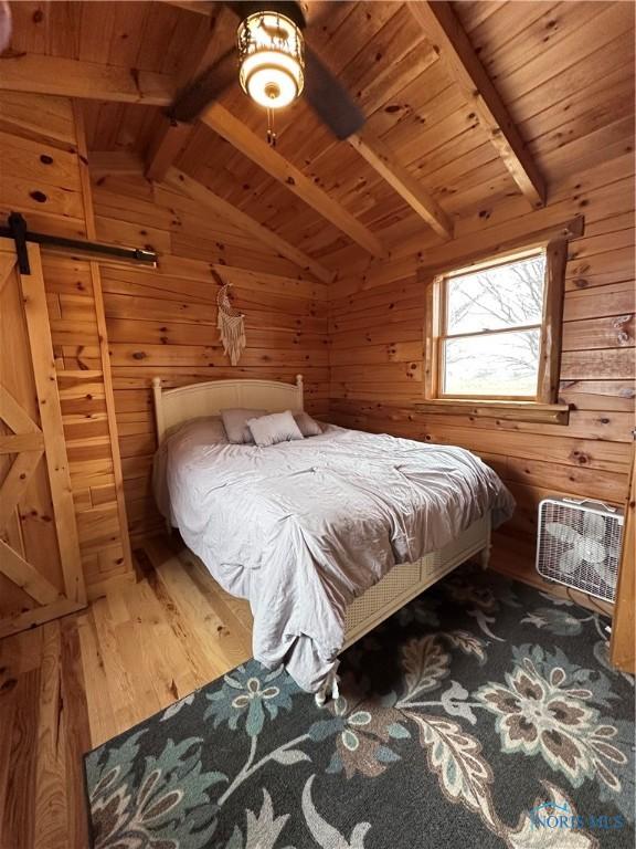 bedroom featuring vaulted ceiling with beams, wood ceiling, wood walls, and a barn door