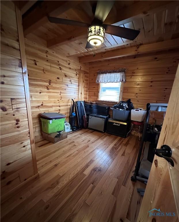 bonus room featuring beamed ceiling, ceiling fan, wood walls, and hardwood / wood-style floors