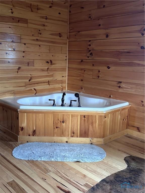 interior space with light wood-style floors, a jacuzzi, and wooden walls