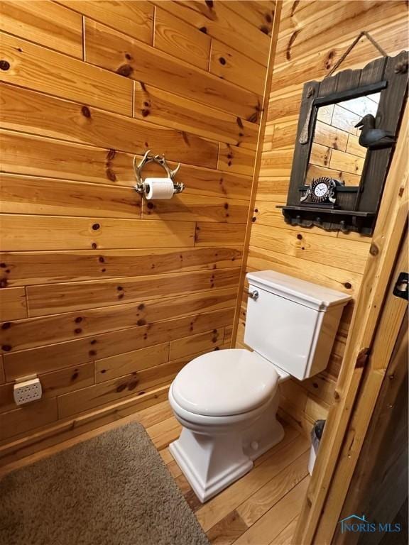 half bathroom with wood walls, wood finished floors, and toilet