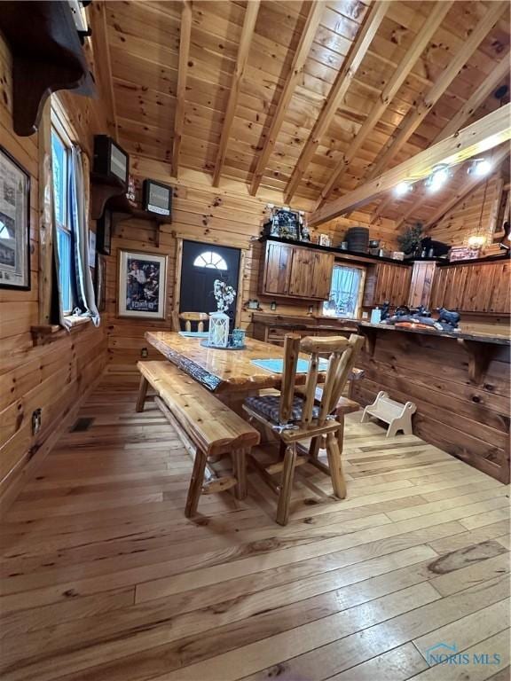 dining space with wooden walls, wood ceiling, lofted ceiling with beams, and hardwood / wood-style floors