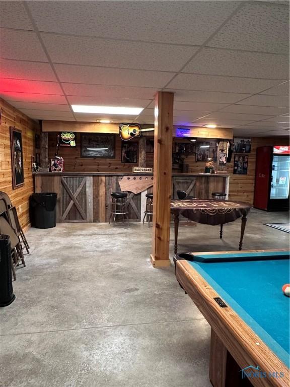 rec room featuring a paneled ceiling, pool table, concrete floors, wood walls, and a bar