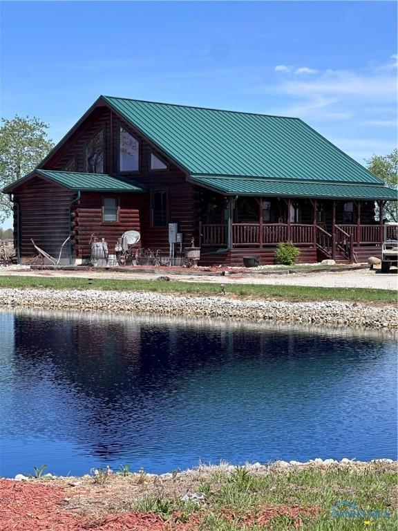 rear view of house featuring log exterior, a porch, a water view, a standing seam roof, and metal roof