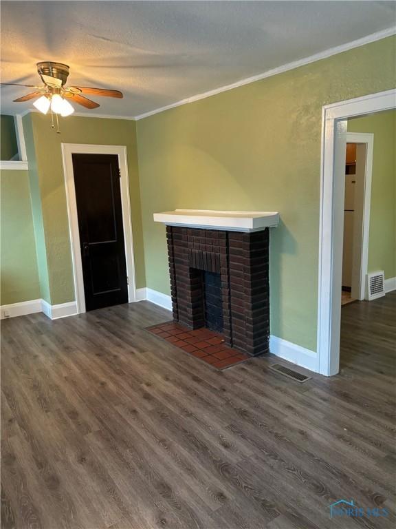 unfurnished living room featuring ceiling fan, dark hardwood / wood-style floors, ornamental molding, and a fireplace