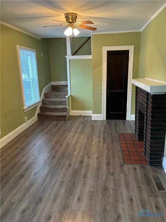 unfurnished living room featuring ceiling fan, dark hardwood / wood-style floors, ornamental molding, and a fireplace