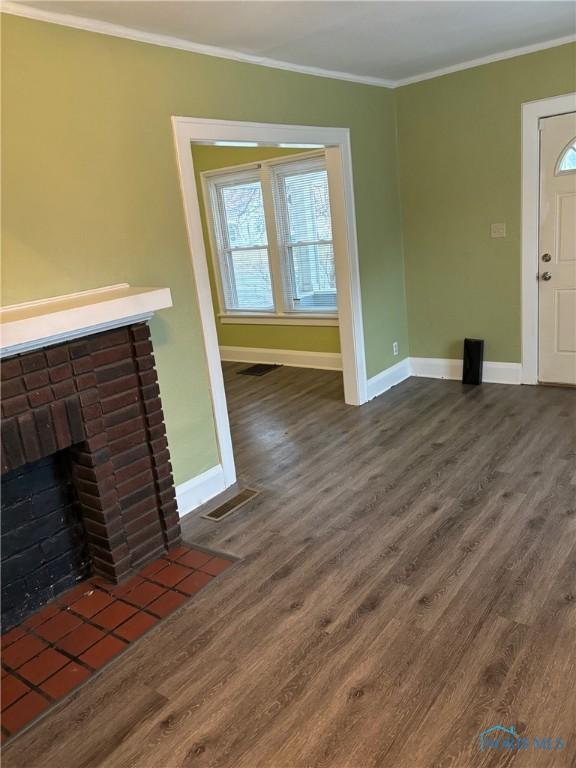 unfurnished living room with a healthy amount of sunlight, dark hardwood / wood-style flooring, ornamental molding, and a fireplace