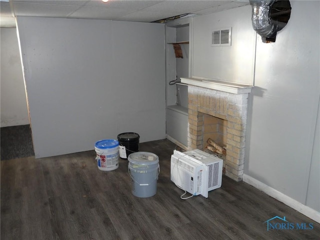 unfurnished living room featuring a paneled ceiling, dark hardwood / wood-style flooring, a wall mounted air conditioner, and a brick fireplace