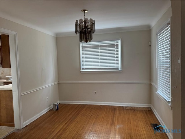 unfurnished dining area with a healthy amount of sunlight, wood-type flooring, and a notable chandelier