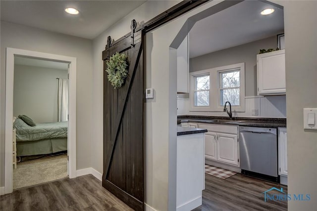 kitchen featuring white cabinets, a barn door, stainless steel dishwasher, and sink