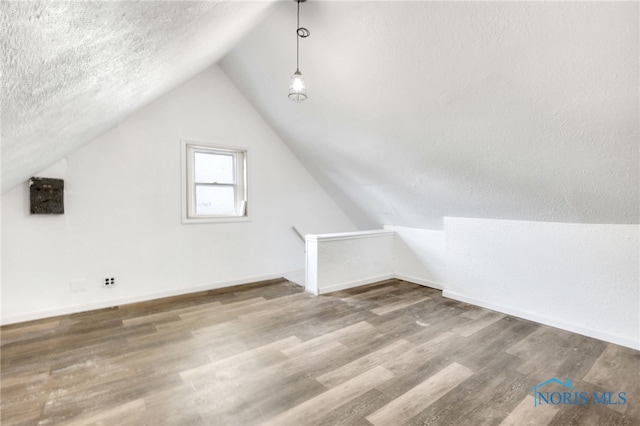 additional living space with lofted ceiling, wood-type flooring, and a textured ceiling